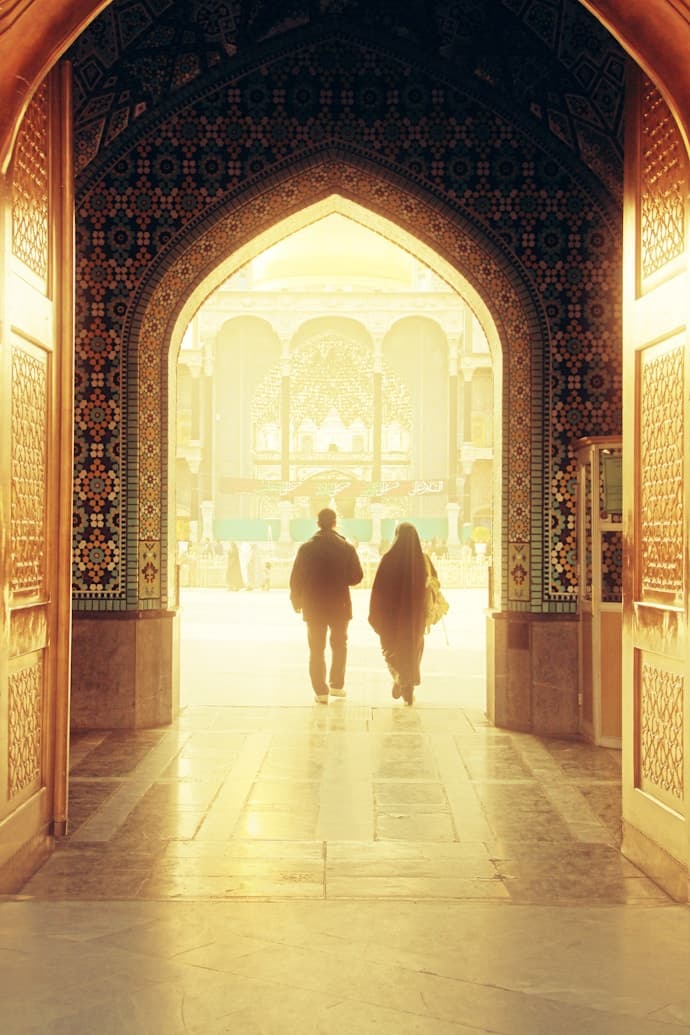 Pilgrims walking through a golden mosque archway